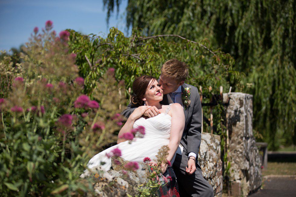 bride and groom sitting on the wall during their coltsford mill wedding