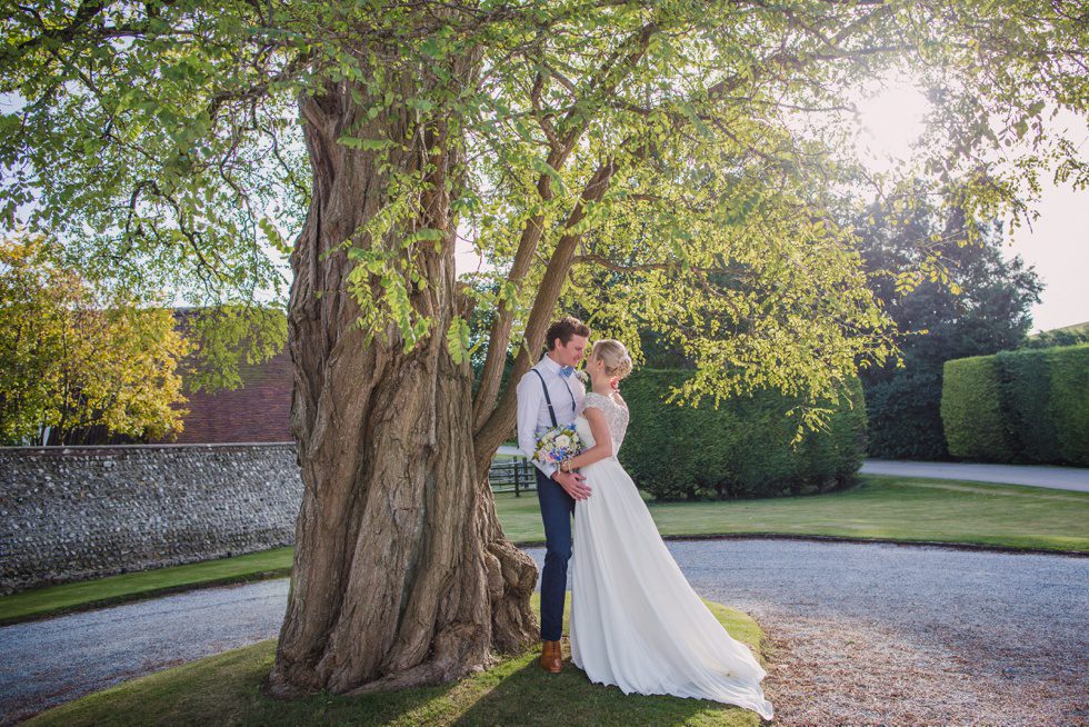 Bride and groom caress under a tree in golden hour light