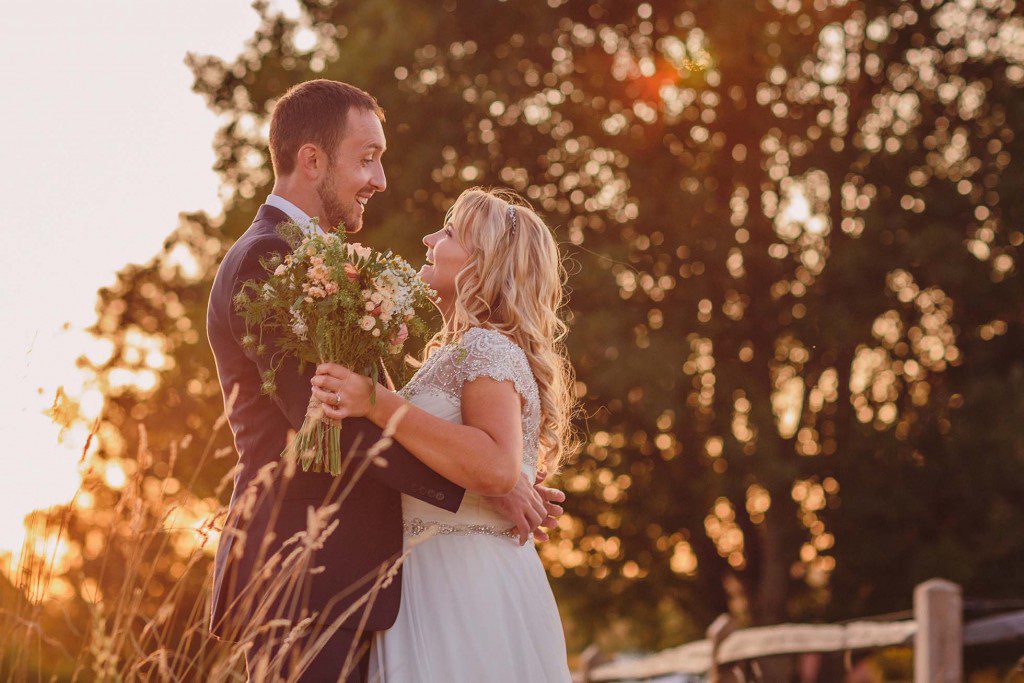 Bride and groom embrace with laughter during golden hour at Grittenham Barn