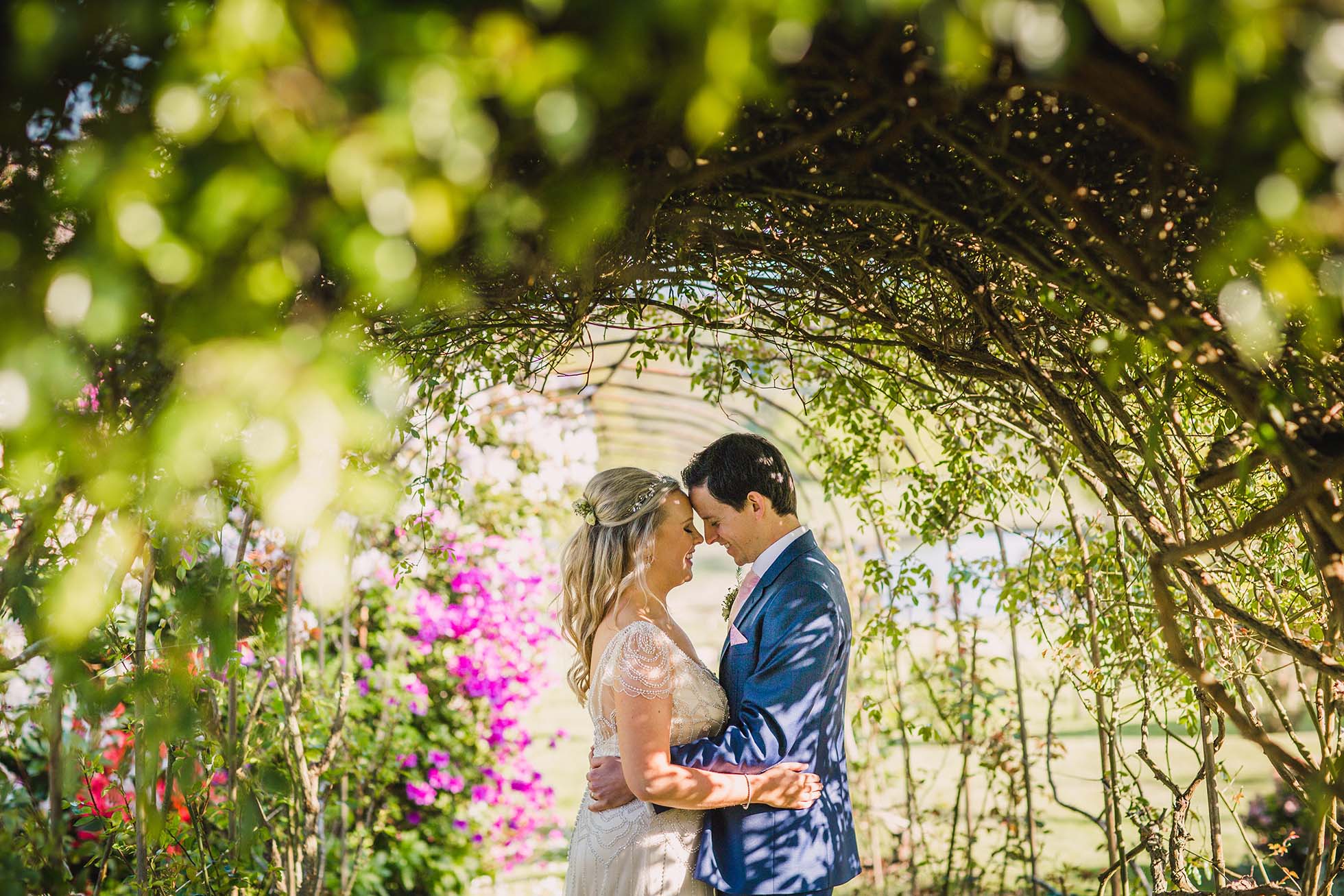 Bride and groom in close embrace under the rose tunnel at Wadhurst Castle