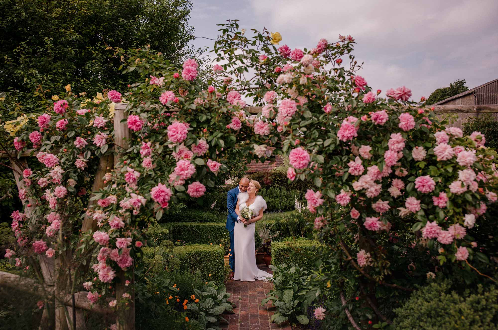 Bride and groom framed under the rambling rose at Pangdean Barn