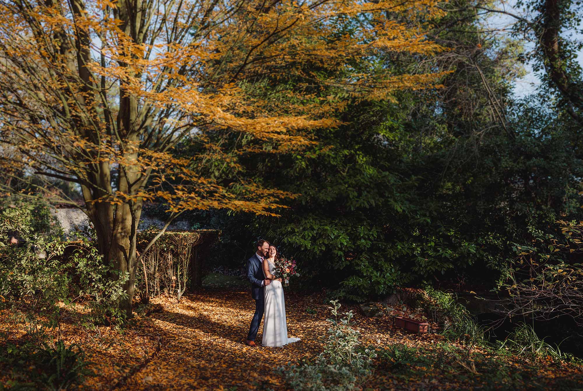 Bride and groom hug amongst the beautiful autumnal tress at St Mary's House Bramber 