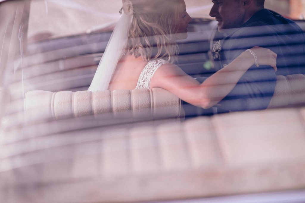 Bride and groom shot through the back of a vintage Mercedes