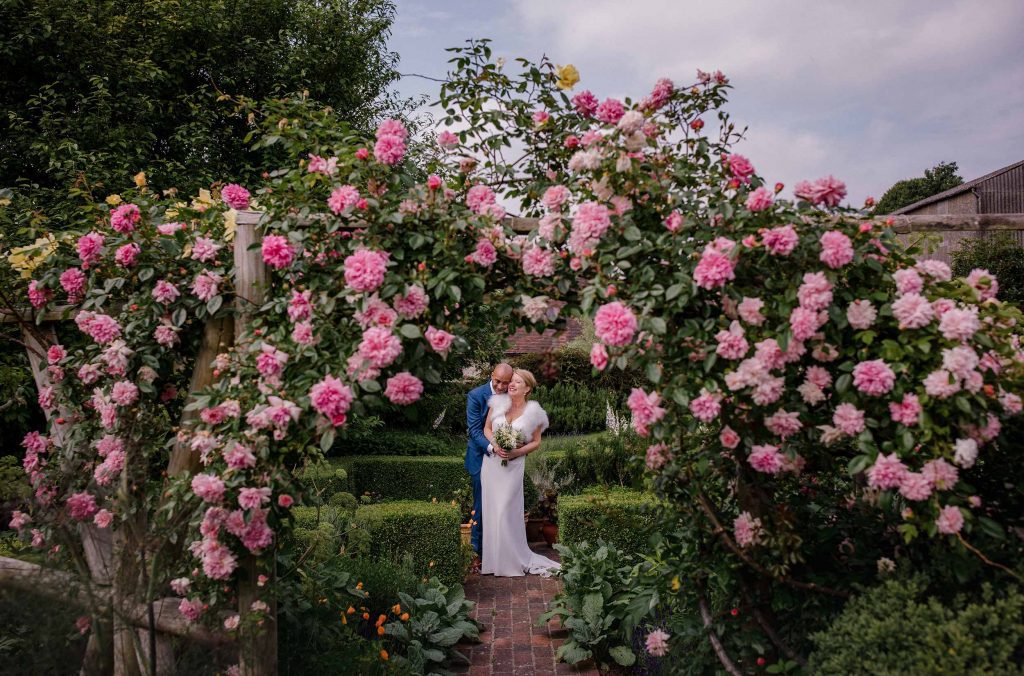 Bride and groom under the rose arch at Pangdean Barn