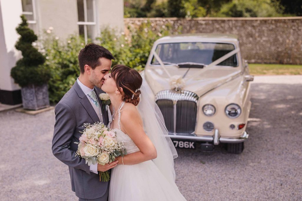 Bride and groom kiss in front of their bridal Rolls Royce