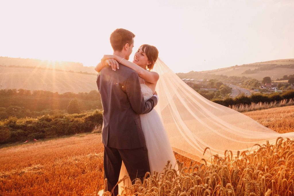 Bride and groom hug at golden hour in amongst the wheat
