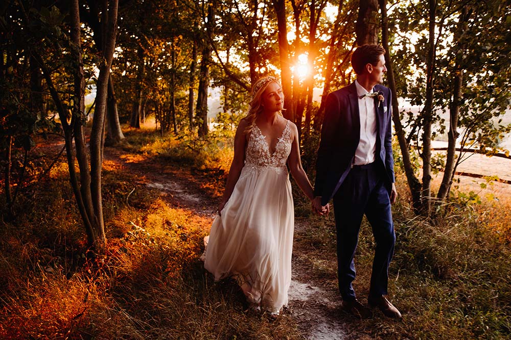 Bride and groom walking through a wood at golden hour at Cissbury Barns