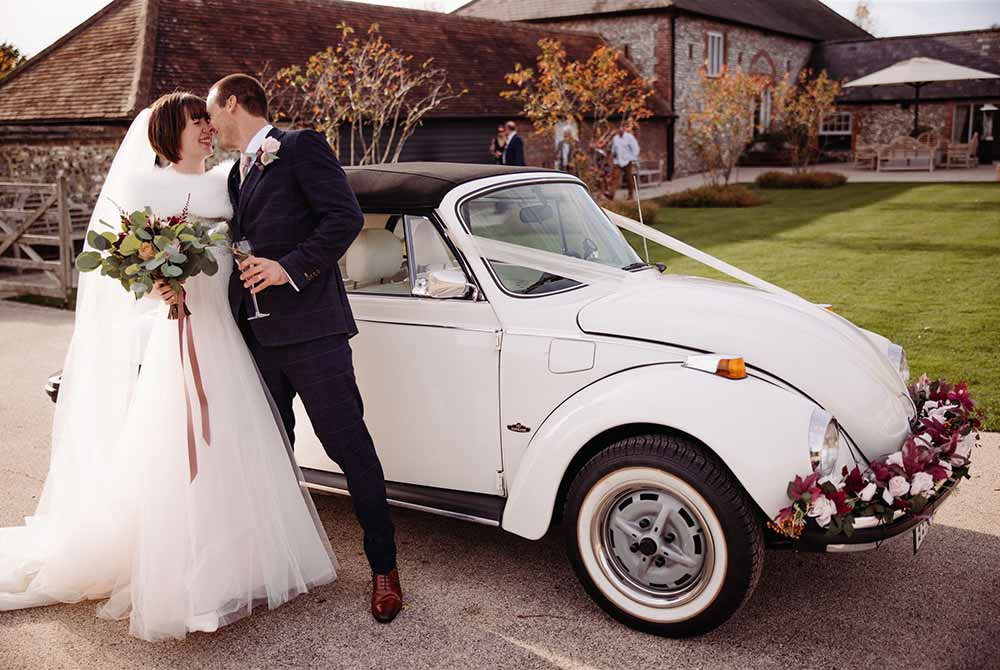 Bride and groom kiss by the side of their vintage VW Beetle at Farbridge  