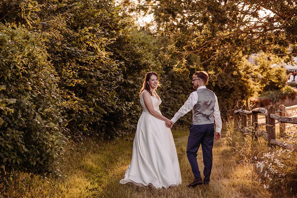 Bride and groom stroll at golden hour in the grounds of Grittenham Barn