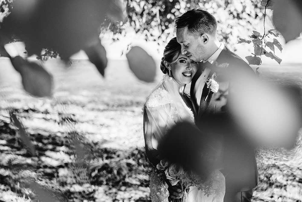 Groom nuzzles bride under a tree